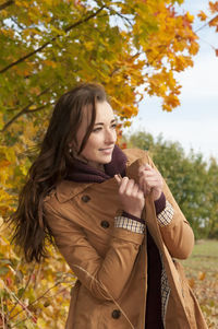 Woman wearing coat standing against trees in park during autumn