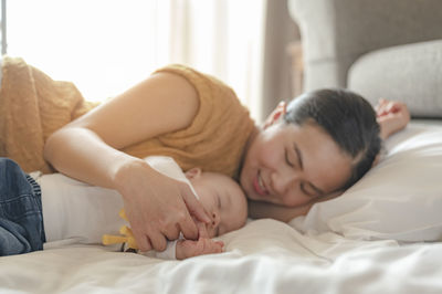 Mother with baby boy sleeping on bed at home