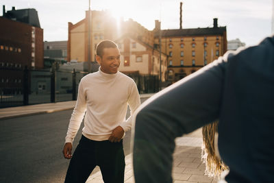 Smiling young man enjoying with friends on sidewalk in city during sunny day