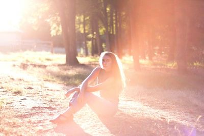 Full length portrait of woman sitting on field during sunny day in park