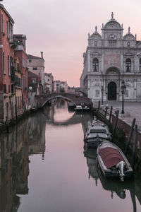 Bridge over canal by buildings against sky during sunset