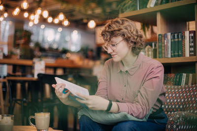 Young woman reading book while sitting at cafe