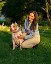 Woman sitting squatting and petting with happy american pitbull terrier at dawn