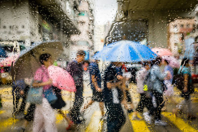 People walking on street seen through wet windshield