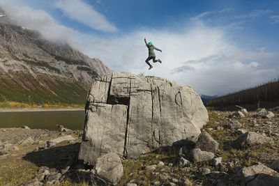 Mid distance view of cheerful woman jumping on rock formation against cloudy sky