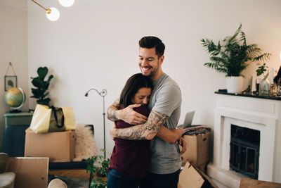 Smiling man embracing woman while standing in living room during relocation