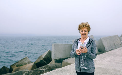 Woman holding camera while standing by sea against clear sky