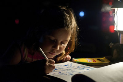 Close-up of girl drawing on book in darkroom at home