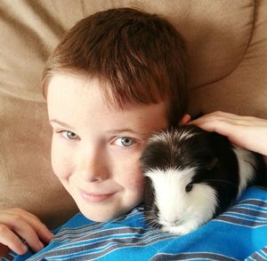 High angle portrait of smiling boy with guinea pig resting on sofa at home