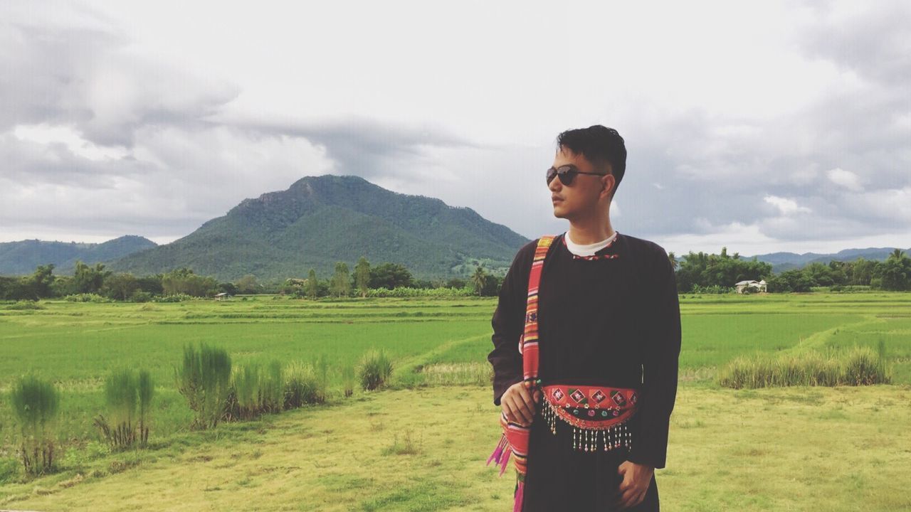 MAN STANDING ON FIELD AGAINST MOUNTAINS