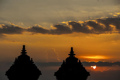 Silhouette temple against building during sunset