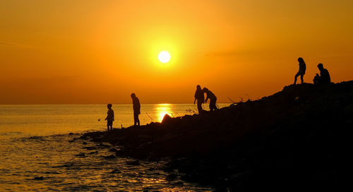 Silhouette people by sea against sky during sunset