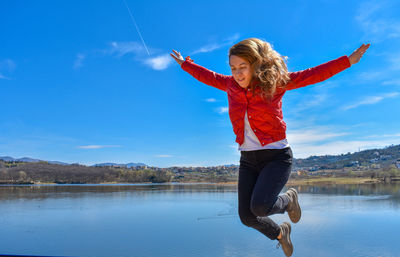 Woman with arms outstretched in lake against sky