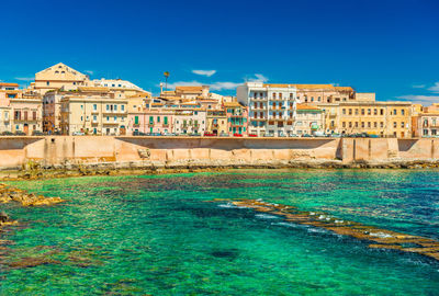 Buildings by sea against clear blue sky