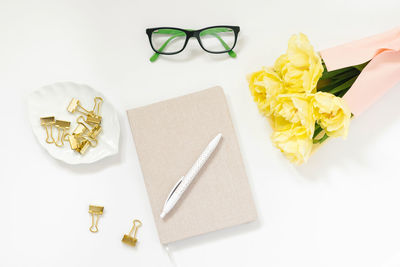 Office desk with a notebook, yellow flowers, clips, white pen with dots for paper, glasses