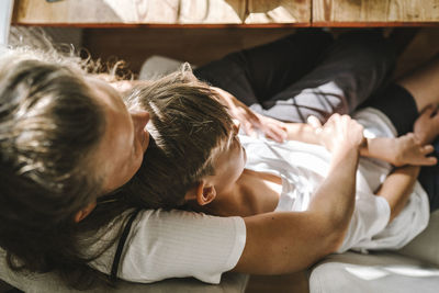 Mother and son lying down on sofa at home during sunny day