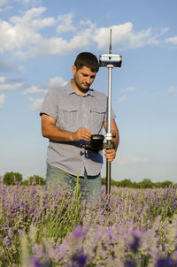 Surveyor with theodolite on lavender field against sky