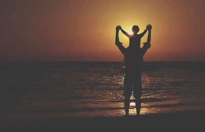 Silhouette woman standing in sea against sunset sky