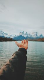 Cropped hand gesturing against lake