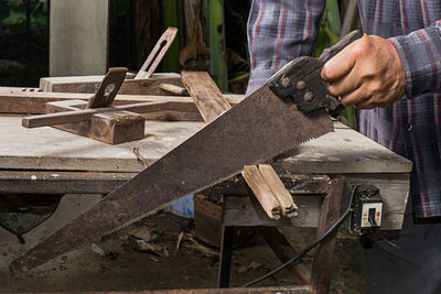 Midsection of worker cutting wood in workshop