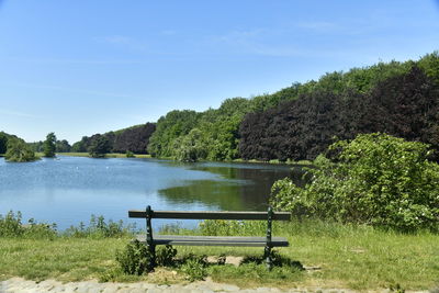 Bench by lake against sky