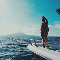 Rear view of young woman standing in boat on sea against sky