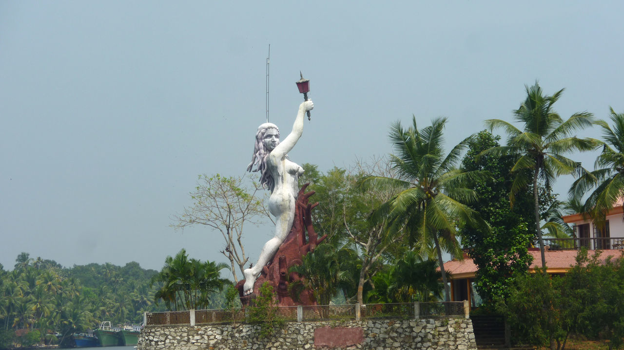 LOW ANGLE VIEW OF STATUE AGAINST TREES AND PLANTS AGAINST SKY