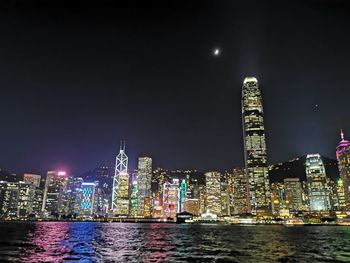 Illuminated buildings by river against sky at night