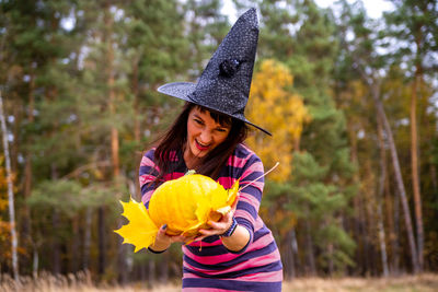 Witch woman holding pumpkin with scary emotions in autumn forest