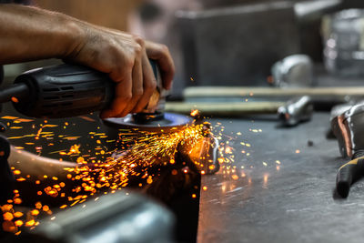 Cropped image of worker using grinder on metal in factory