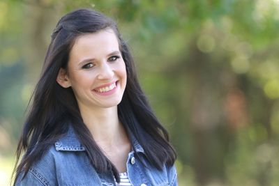 Portrait of smiling young woman against trees