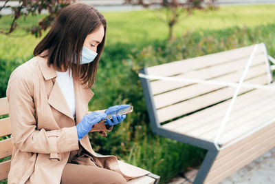 Woman in protective  mask and gloves using smartphone. physical social distancing.