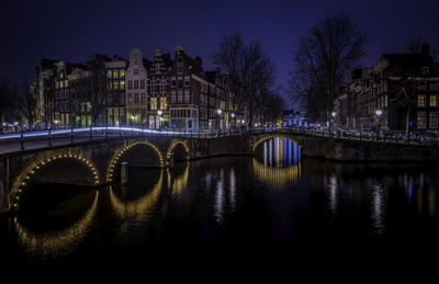 Arch bridge over river in city at night