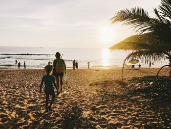 Rear view of people walking on beach against sky during sunset