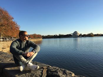 Man sitting by lake against clear sky