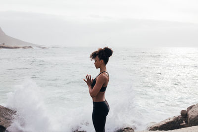 Side view of young woman standing at beach against sky