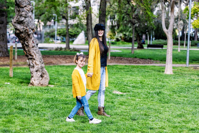 Portrait of mother and daughter holding hands while walking on grassy field in park