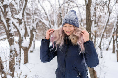 Smiling young woman wearing warm clothing standing on snow in forest