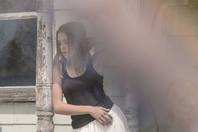 Young woman looking down while standing in porch