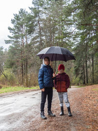 Two brothers stand under one umbrella