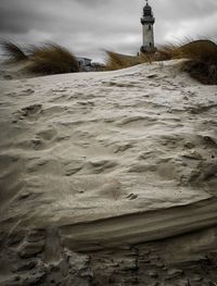 Lighthouse on beach by buildings against sky