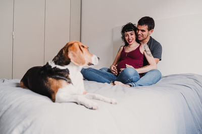 Pregnant woman smiling with male partner while dog sitting on bed