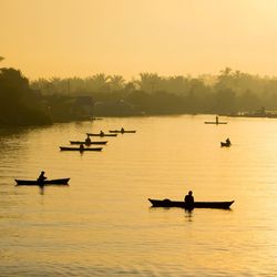 Silhouette people on river against sky during sunrise