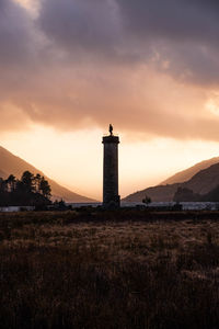 Lighthouse on field against sky during sunset