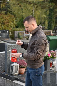 Side view of man holding tea light candle while standing in cemetery