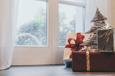 Gift boxes on floor near the door and christmas tree inside home. box with holiday ribbon with bows