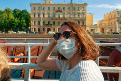 A girl in sunglasses and a white medical mask is sitting on the boat, waiting for departure. 