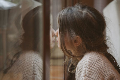 Close-up of cute girl looking through window at home