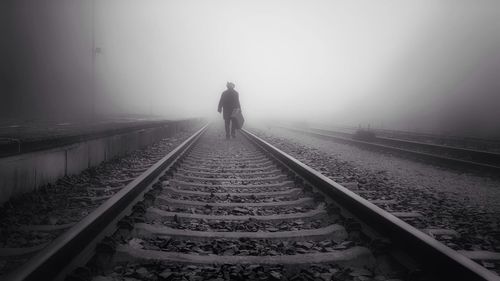 Rear view of person on railroad tracks during foggy weather