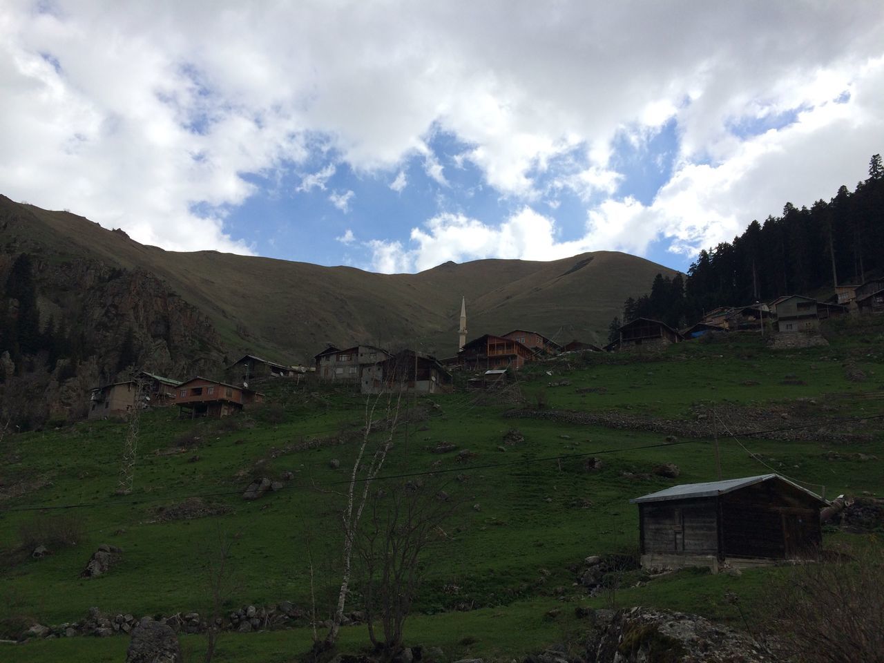 mountain, sky, landscape, house, built structure, cloud - sky, architecture, mountain range, building exterior, grass, tranquil scene, field, tranquility, rural scene, cloud, nature, village, scenics, cloudy, beauty in nature